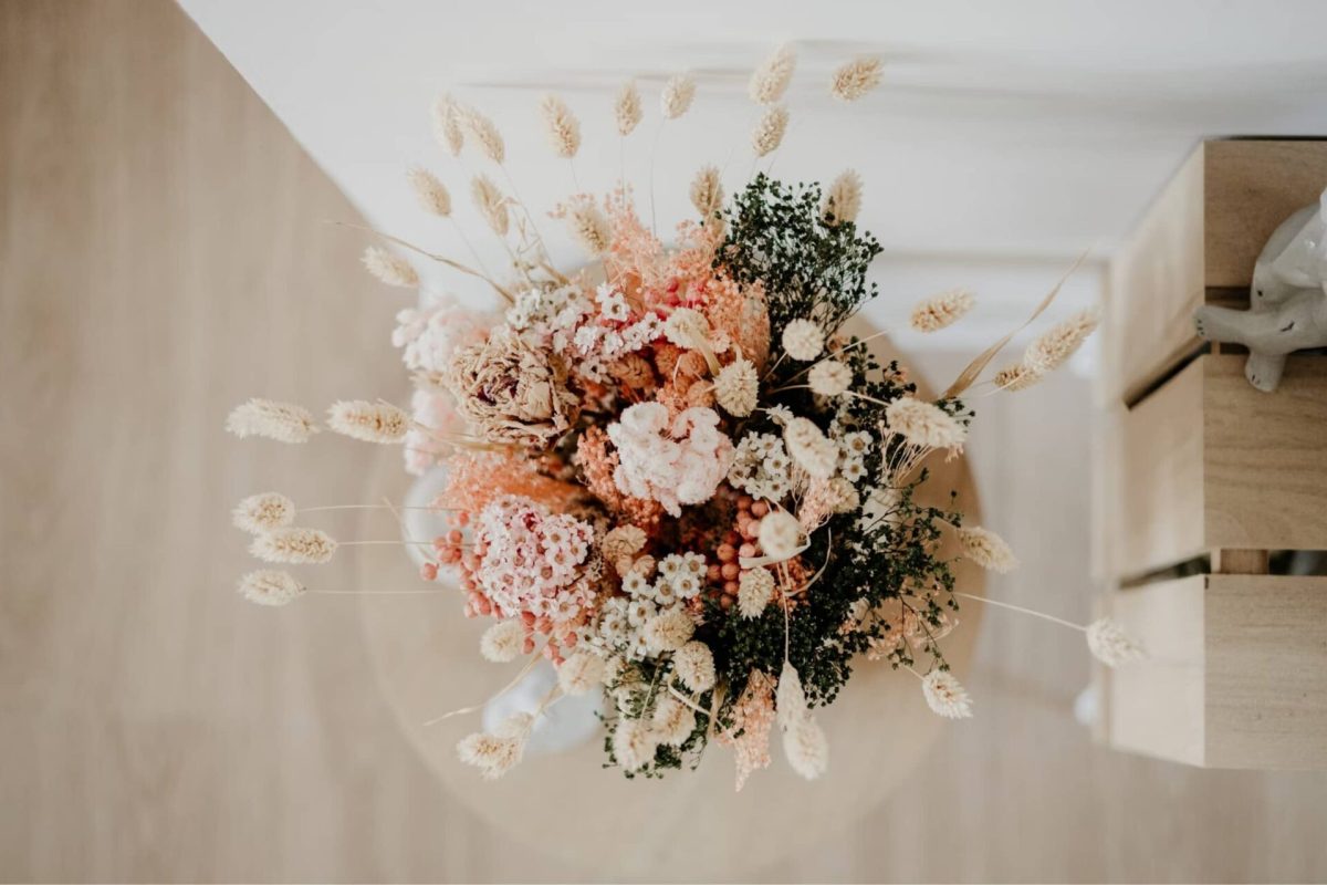 Dried flower bouquet in soft pinks and creams arranged in a vase against a wooden backdrop.