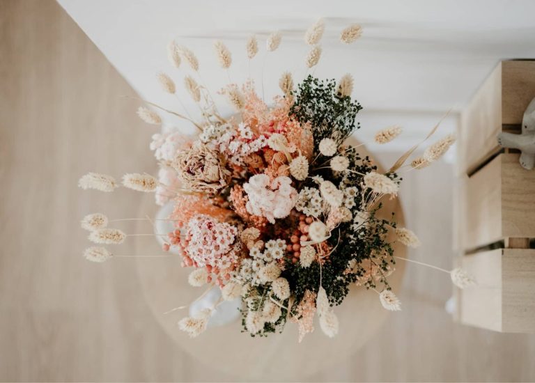 Dried flower bouquet in soft pinks and creams arranged in a vase against a wooden backdrop.